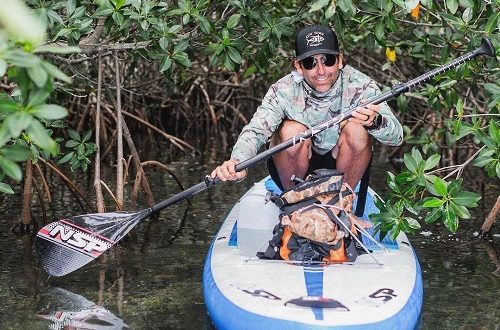 man in a kayak with a watershed dry bag paddling through some low bushes