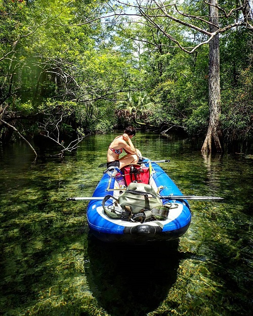 women on a raft in a swampy area with vibrant tress around and a drybag in the boat