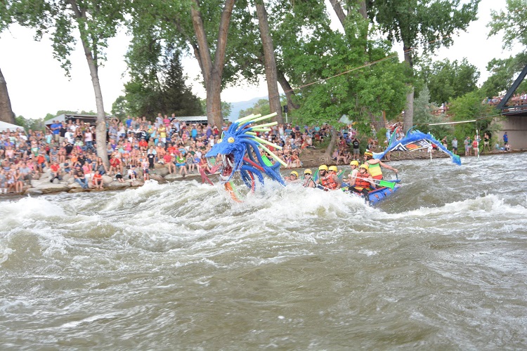 Dragon raft floating down the river as people cheer on the sideline, image from Royal Gorge Whitewater Festival