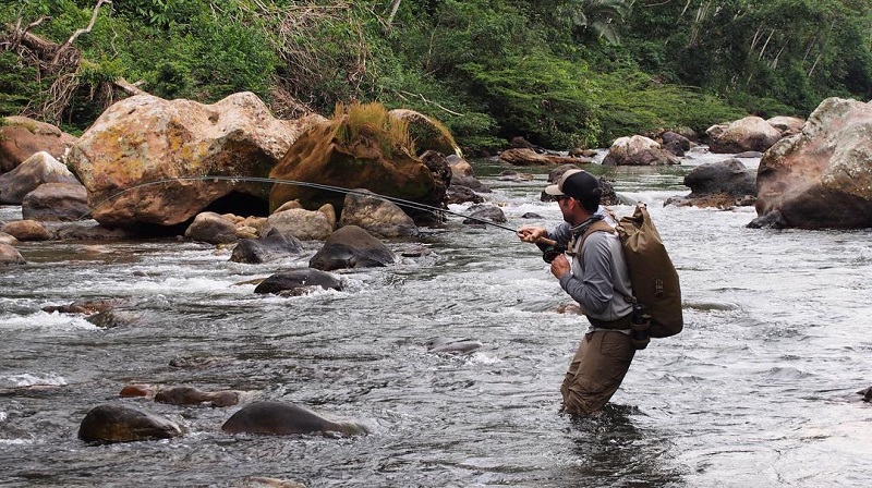 Man fishing in the river with the water knee level wearing a Big Creek Drybag