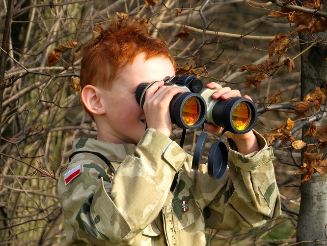 Person holing binoculars wearing camo attire in the woods. 