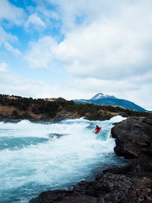 Photo by Dylan McKinney in Patagonia kayaking down the blue river with a mountain peak in the background