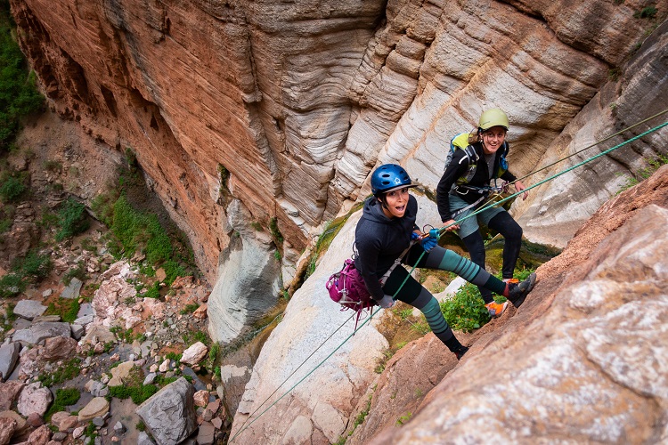2 women canyoneering down a rock face 