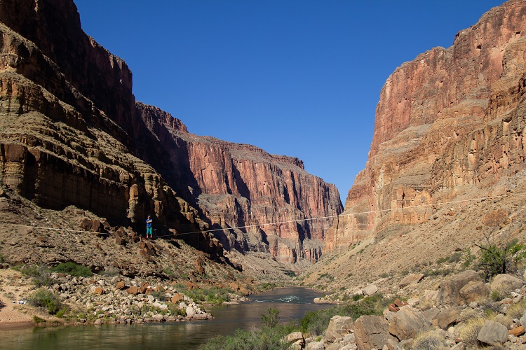 Person standing on a slack line over the river with canyon walls all around 