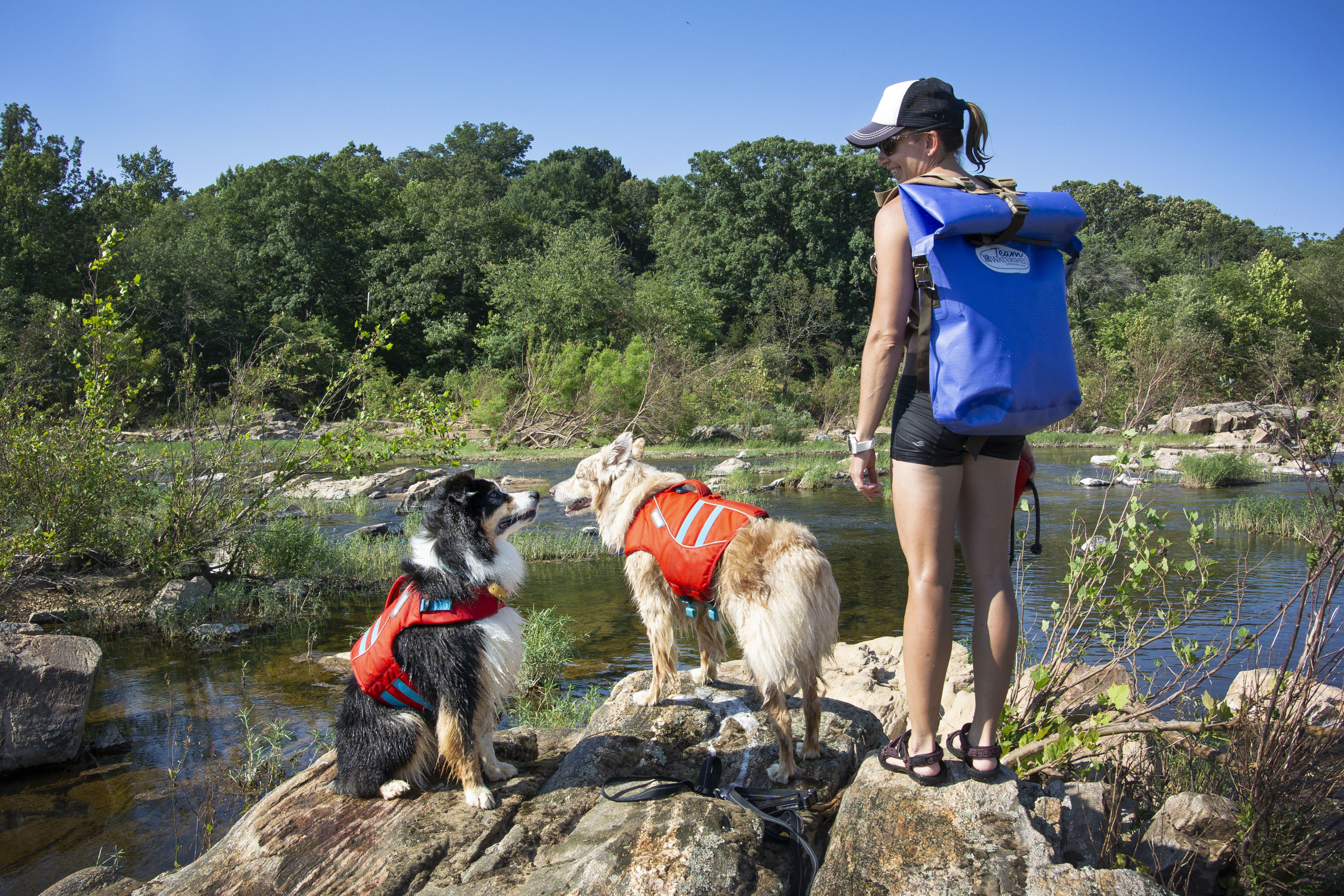 Women with a Watershed drybag backpack on and two dogs standing next to her by the river