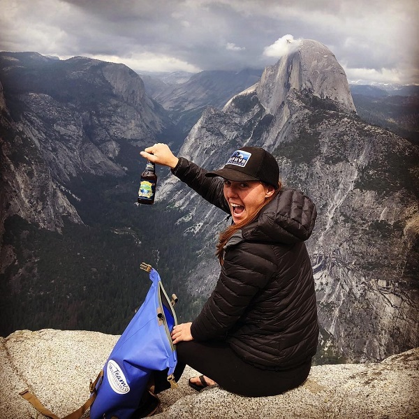 Women pulling a beer from a Watershed Drybag on the edge of a cliff with mountain views in the background