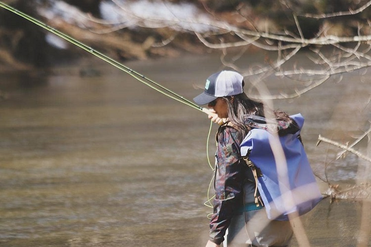 Laurel Monaghan holding a fishing pole with a big creek backpack in the water. 