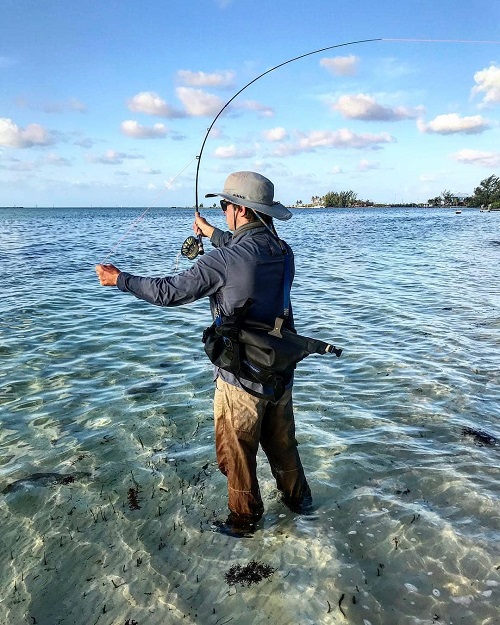 Man fishing in clear blue water with a watershed drybag on his shoulder 