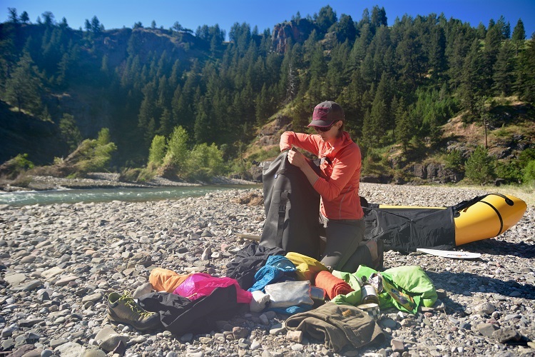 Packing an Animas backpack with clothes and necessities on the bank of the river