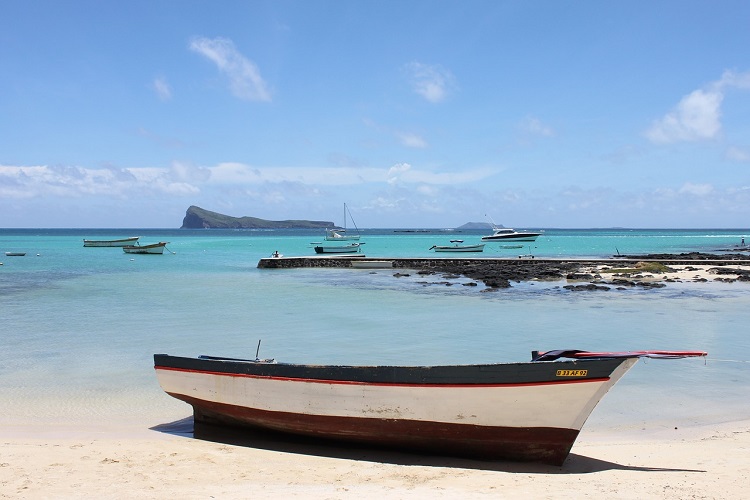 Fishing boat sitting on the sandy shore next to crystal blue water