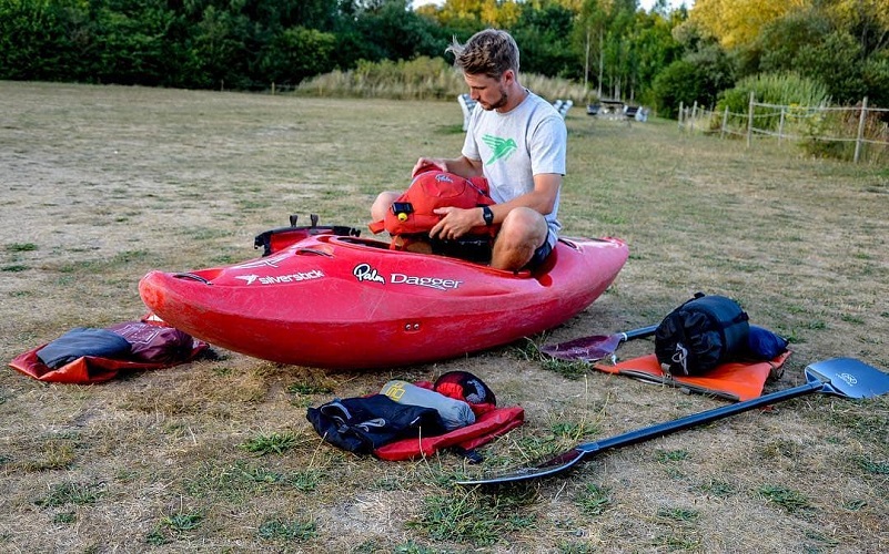 Man sitting in a kayak on dry land packing his drybag for the day 