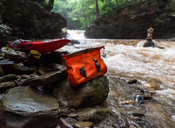 Ocoee Drybag sitting on a rock next to the river with a kayak in the background