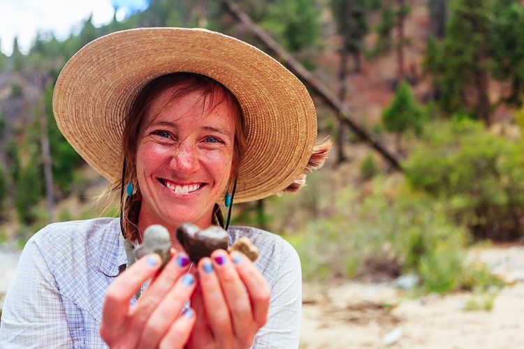Women holding heart rocks on a beach wearing a sunhat