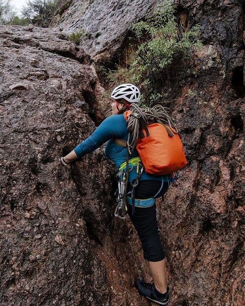 Rock climber with a Watershed Drybags backpack on scaling a wall