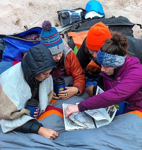 Four people huddled over a map outside wearing winter gear