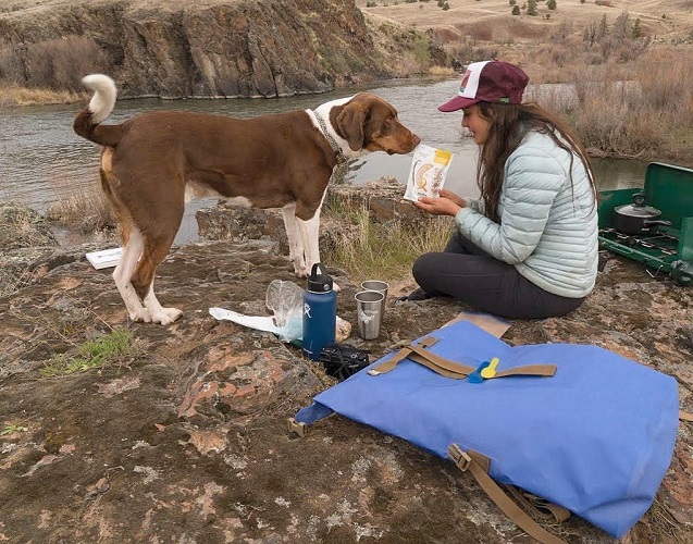 Person and her dog sitting outside making some snacks next to a Watershed Drybag