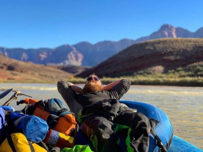 Man relaxing on a raft as he floats down the river with canyons in the background
