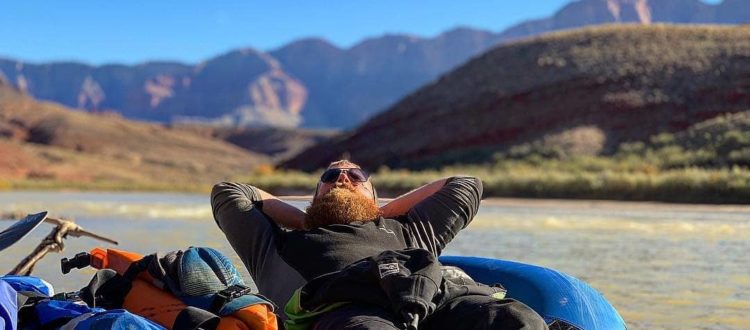 Man relaxing on a raft as he floats down the river with canyons in the background